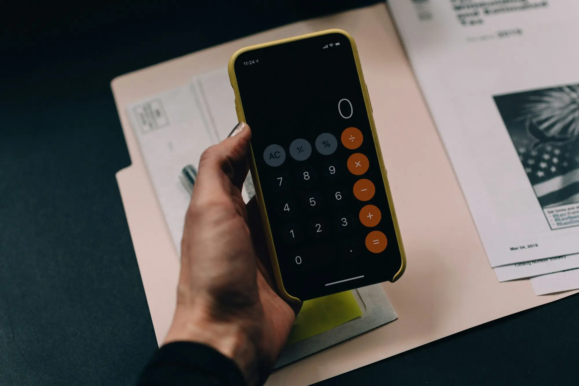 Hand holding a smartphone calculator over paperwork