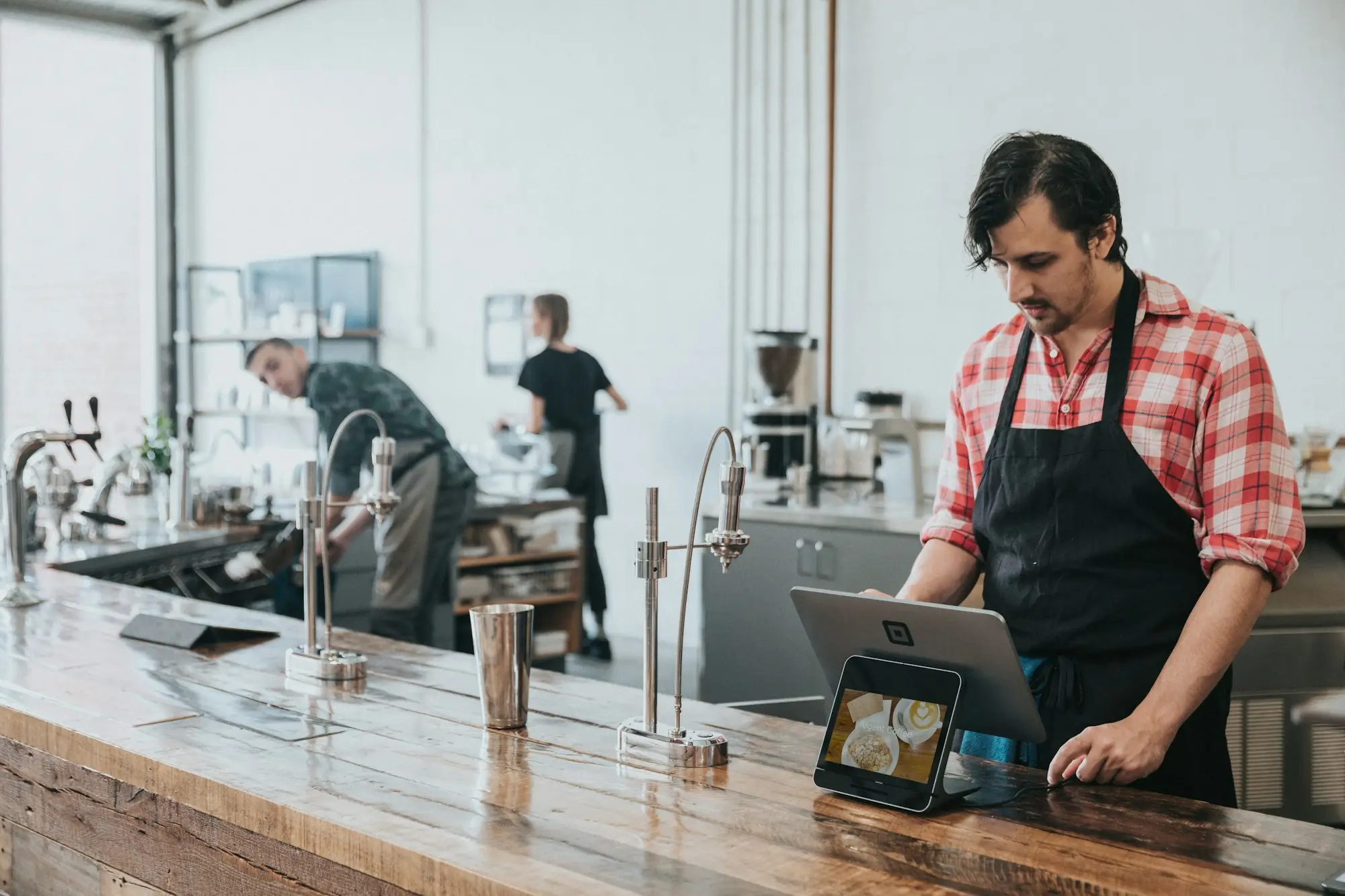 Barista in an apron using a tablet at a wooden counter