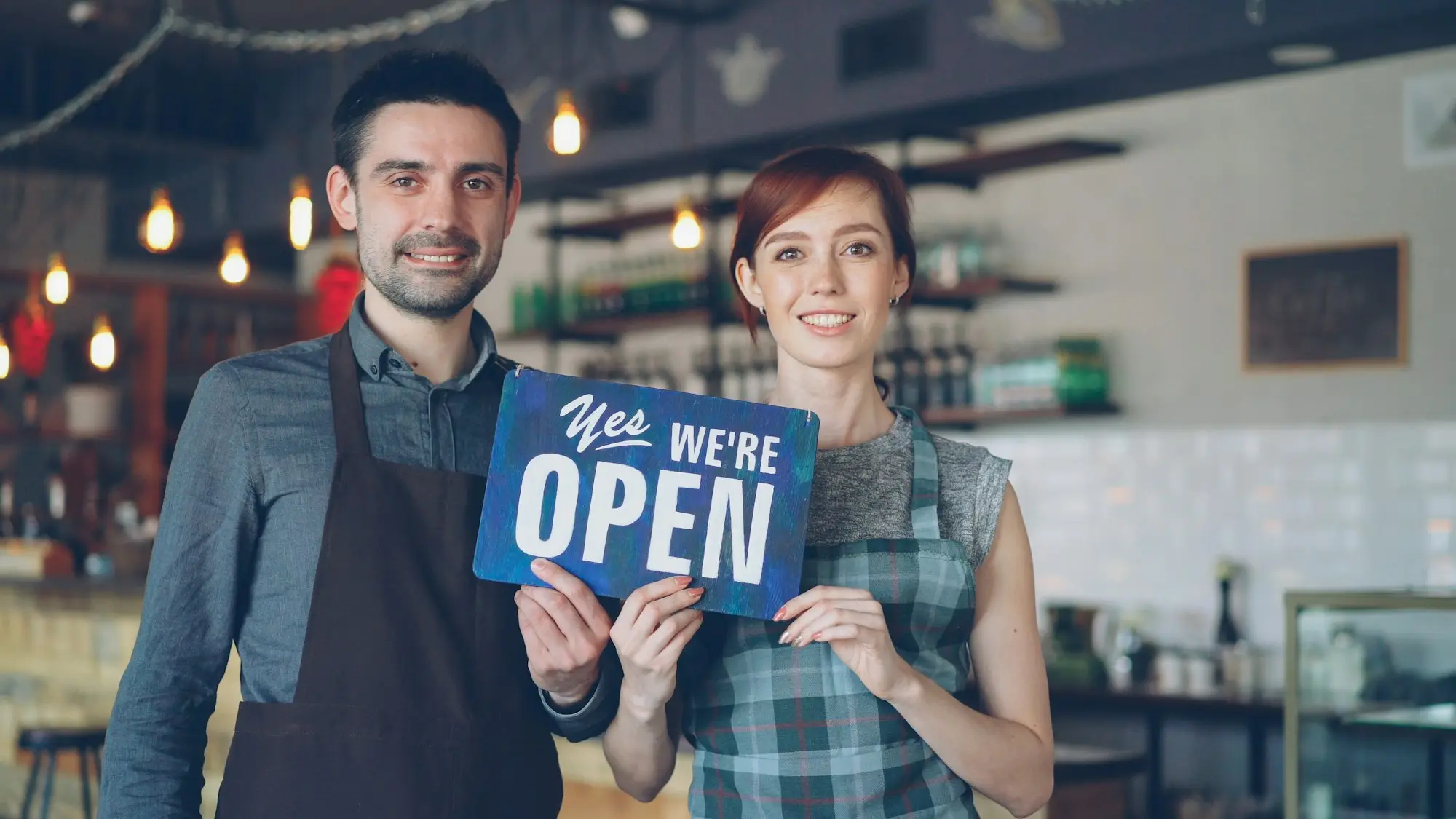 Smiling business owners holding an open sign